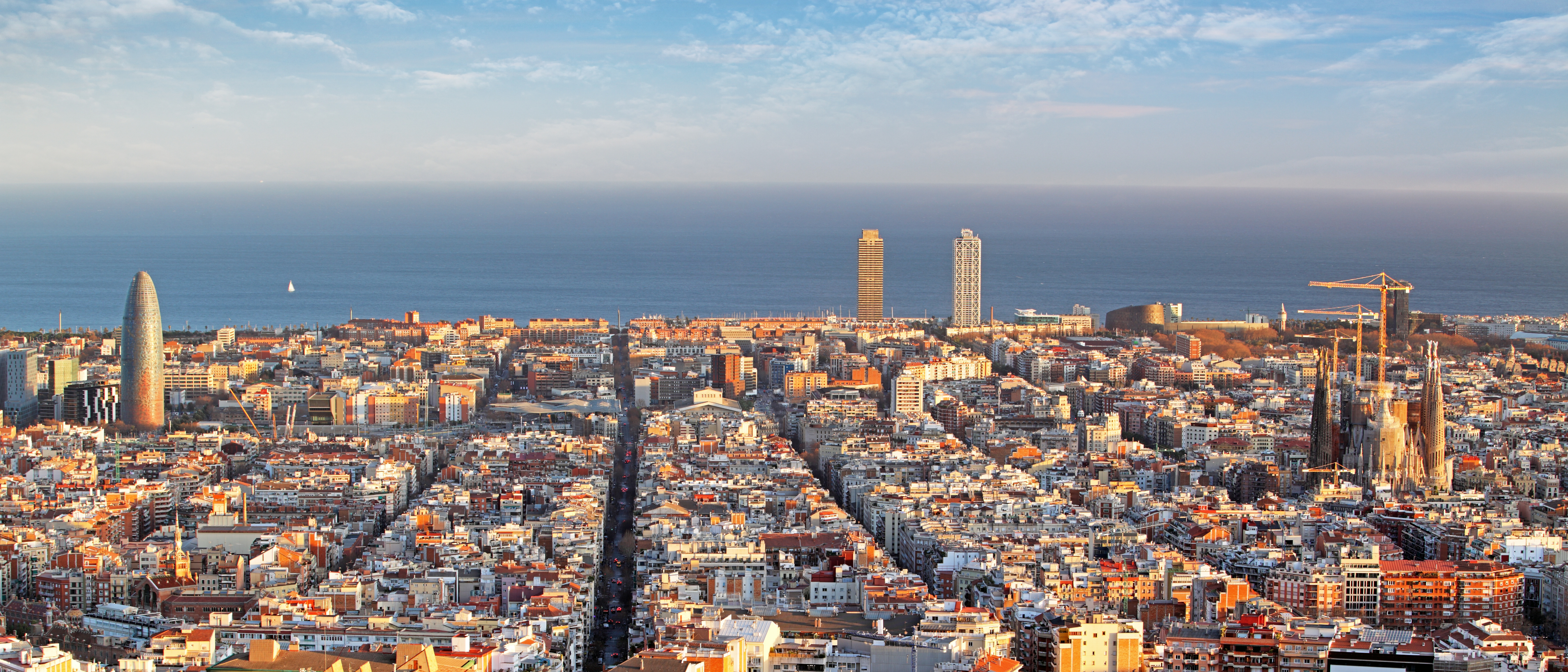 Aerial view of Barcelona's cityscape with distinctive buildings, dense urban development, and Mediterranean Sea horizon.