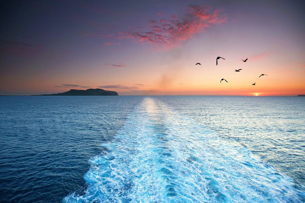 Sunset over Mediterranean Sea with birds flying and distant island on horizon.