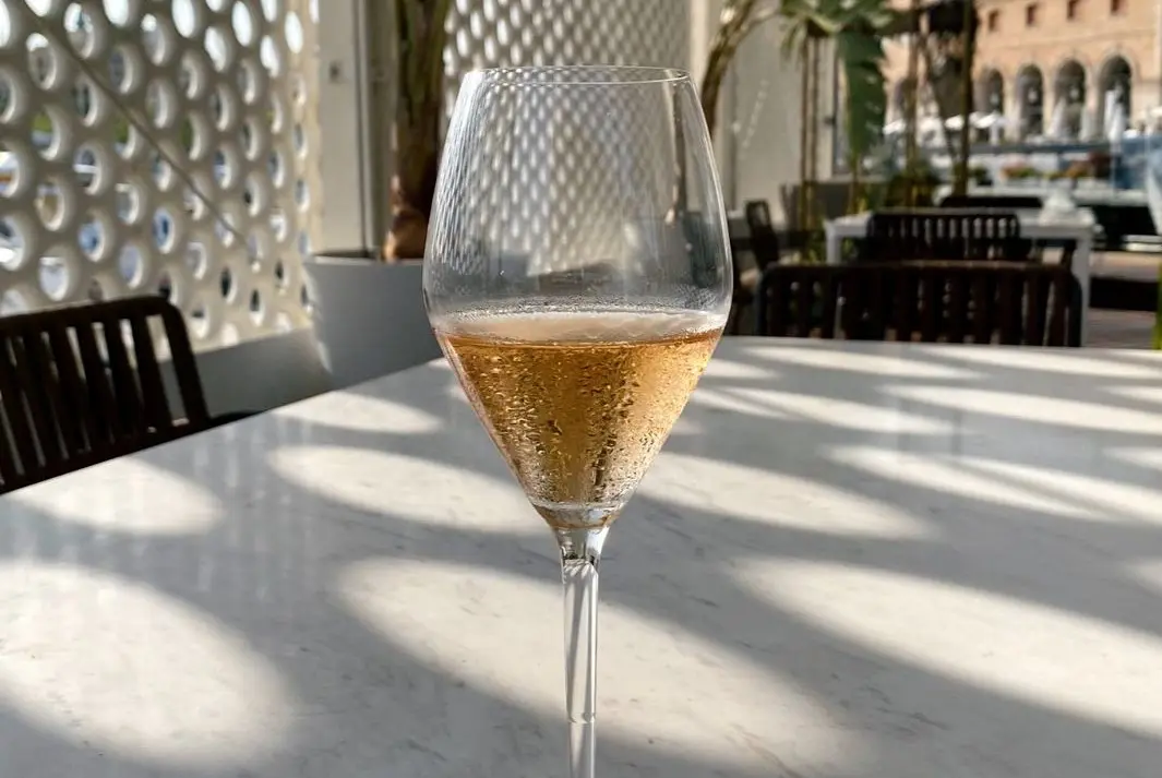 Glass of sparkling wine on a sunny waterfront terrace with architectural details.