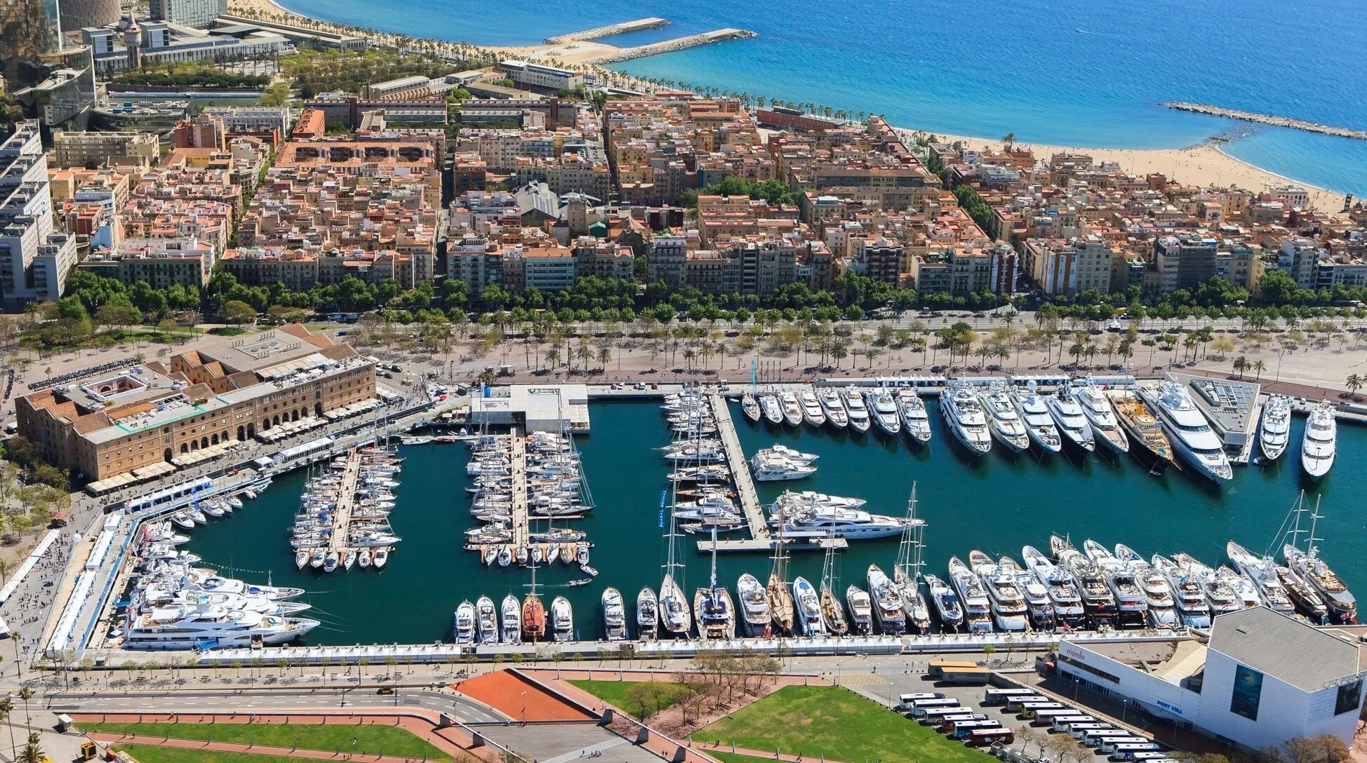 Aerial view of Marina Port Vell with numerous moored superyachts, Barcelona cityscape and Mediterranean Sea.