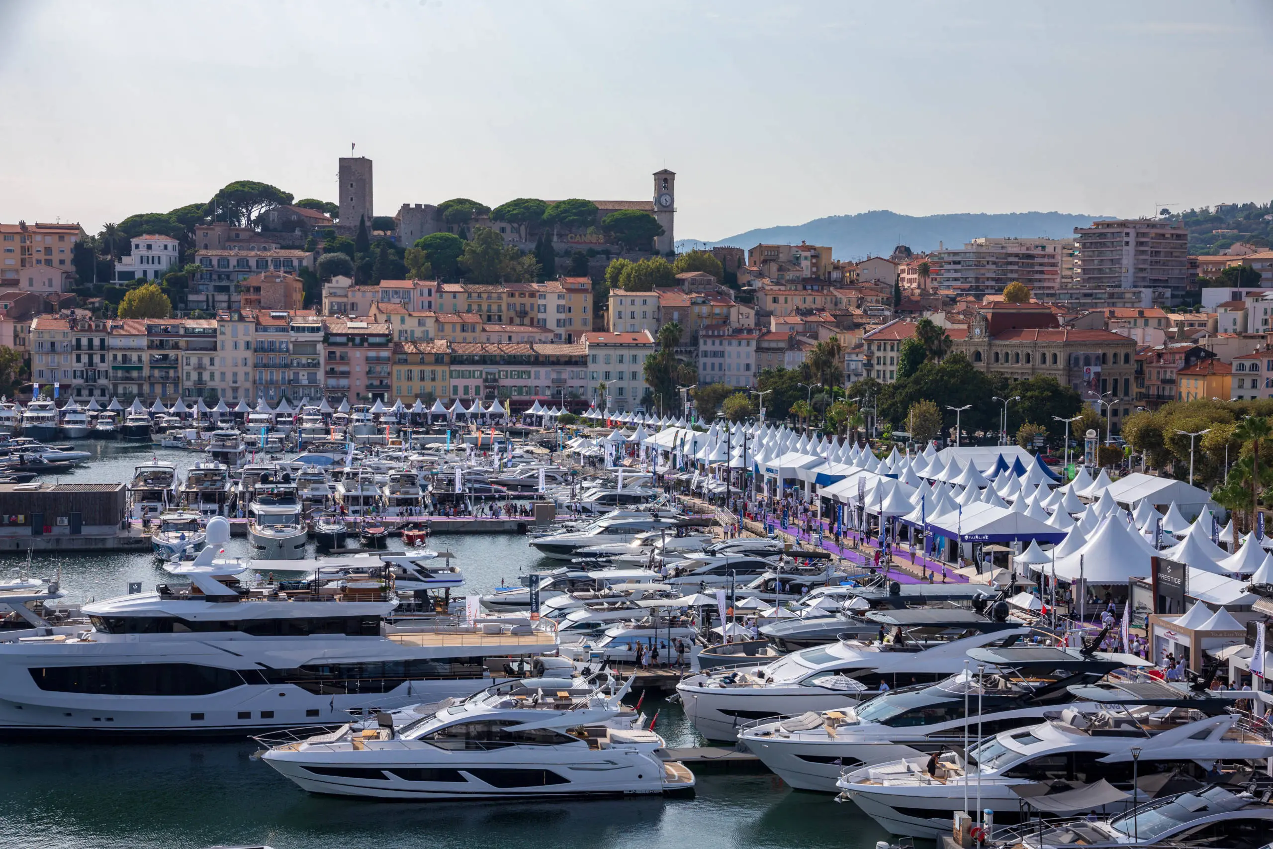 Superyachts and boats moored at Marina Port Vell with Barcelona's waterfront cityscape and hills in the background.