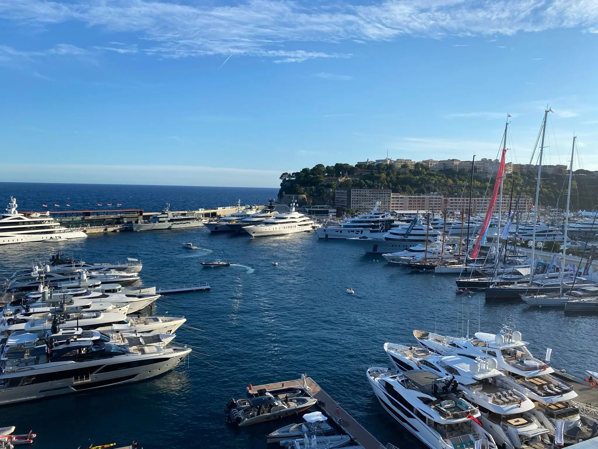 Superyachts and sailing boats moored in Barcelona marina with hillside buildings and clear blue sea.