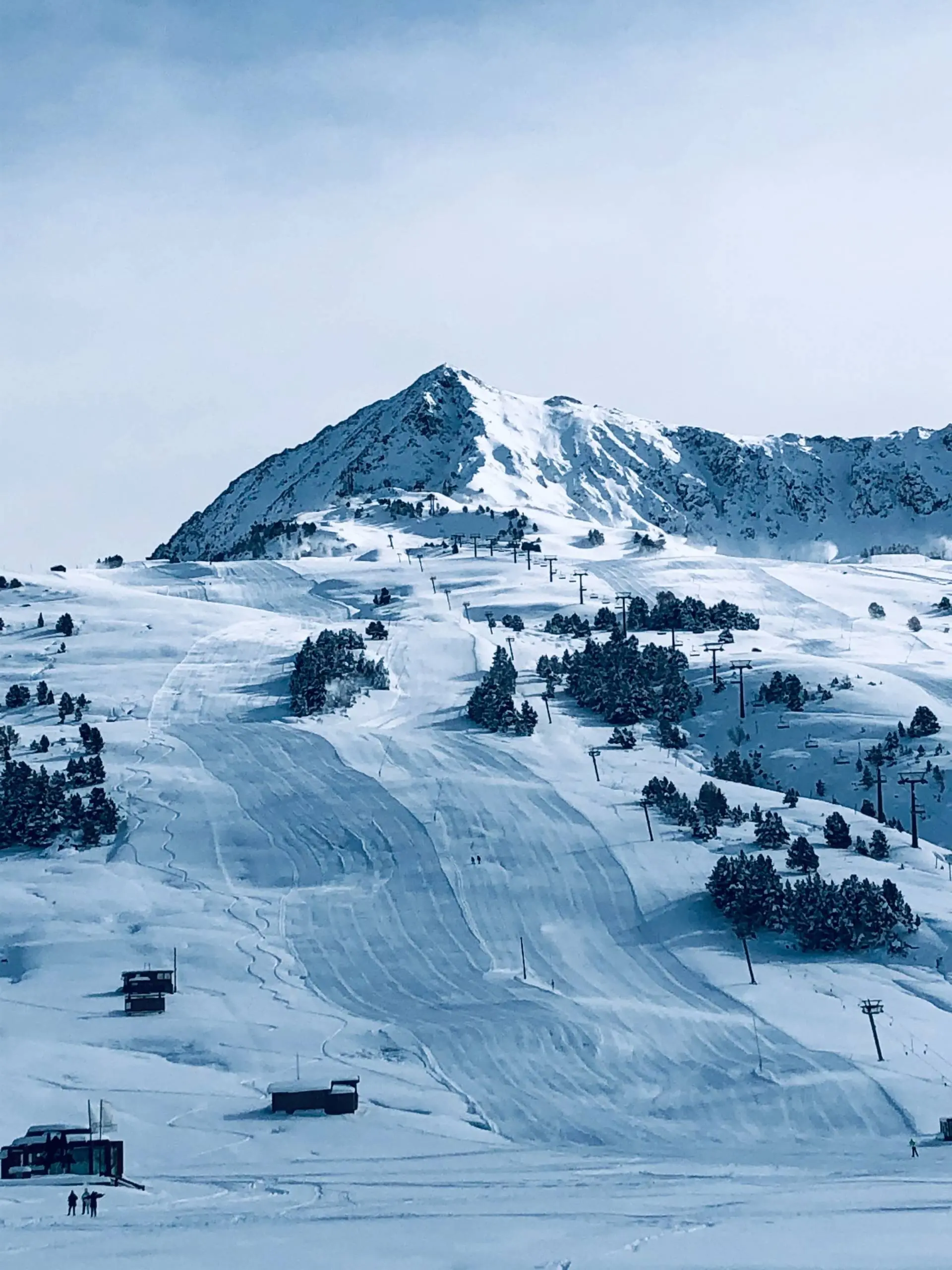 Snow-covered ski resort with ski runs, lift infrastructure, and a snow-capped mountain peak in the background.
