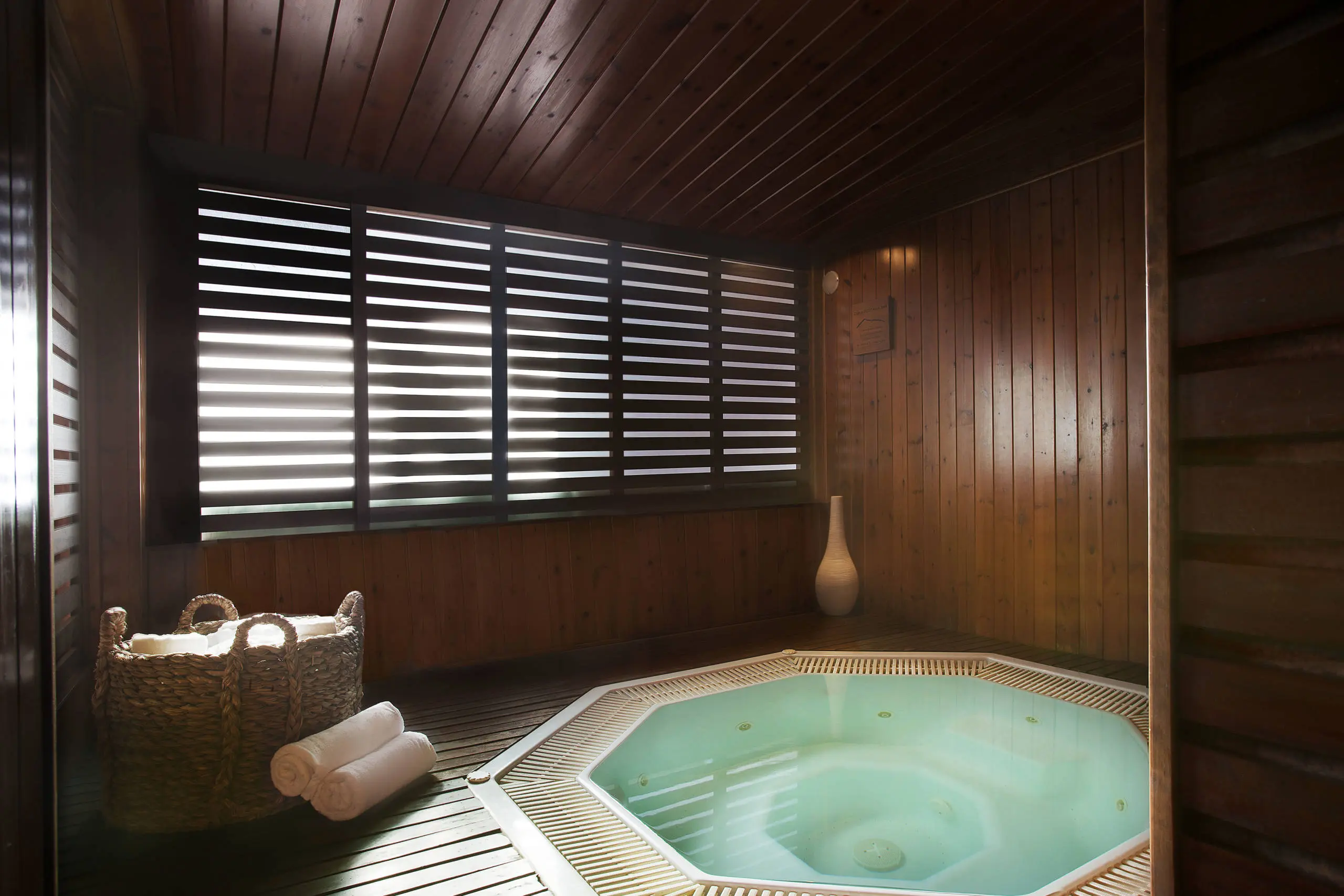 Indoor spa with turquoise soaking tub, wooden paneling, and louvered windows allowing natural light.