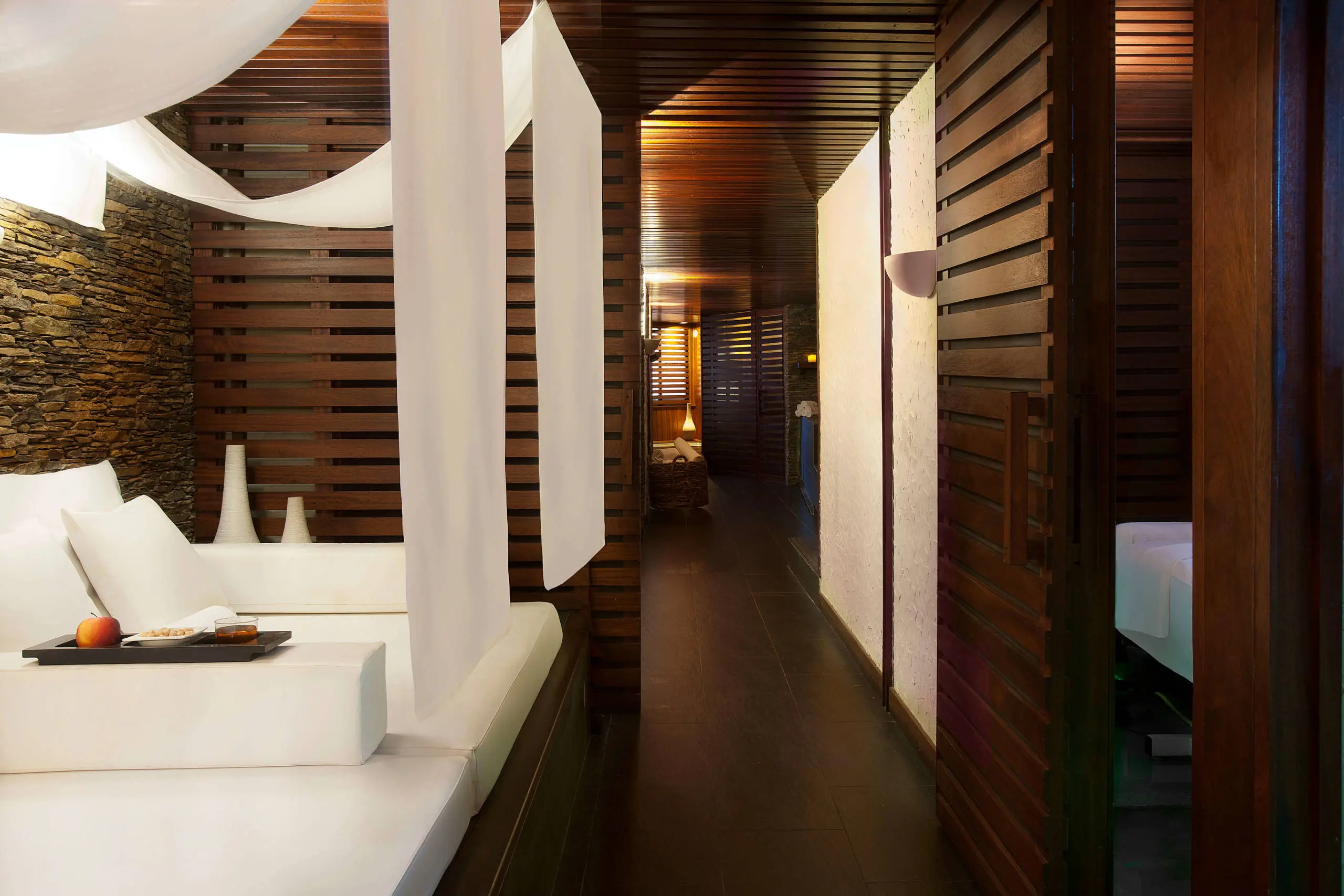 Modern interior hallway with white walls, dark wood slats, and seating area on left.