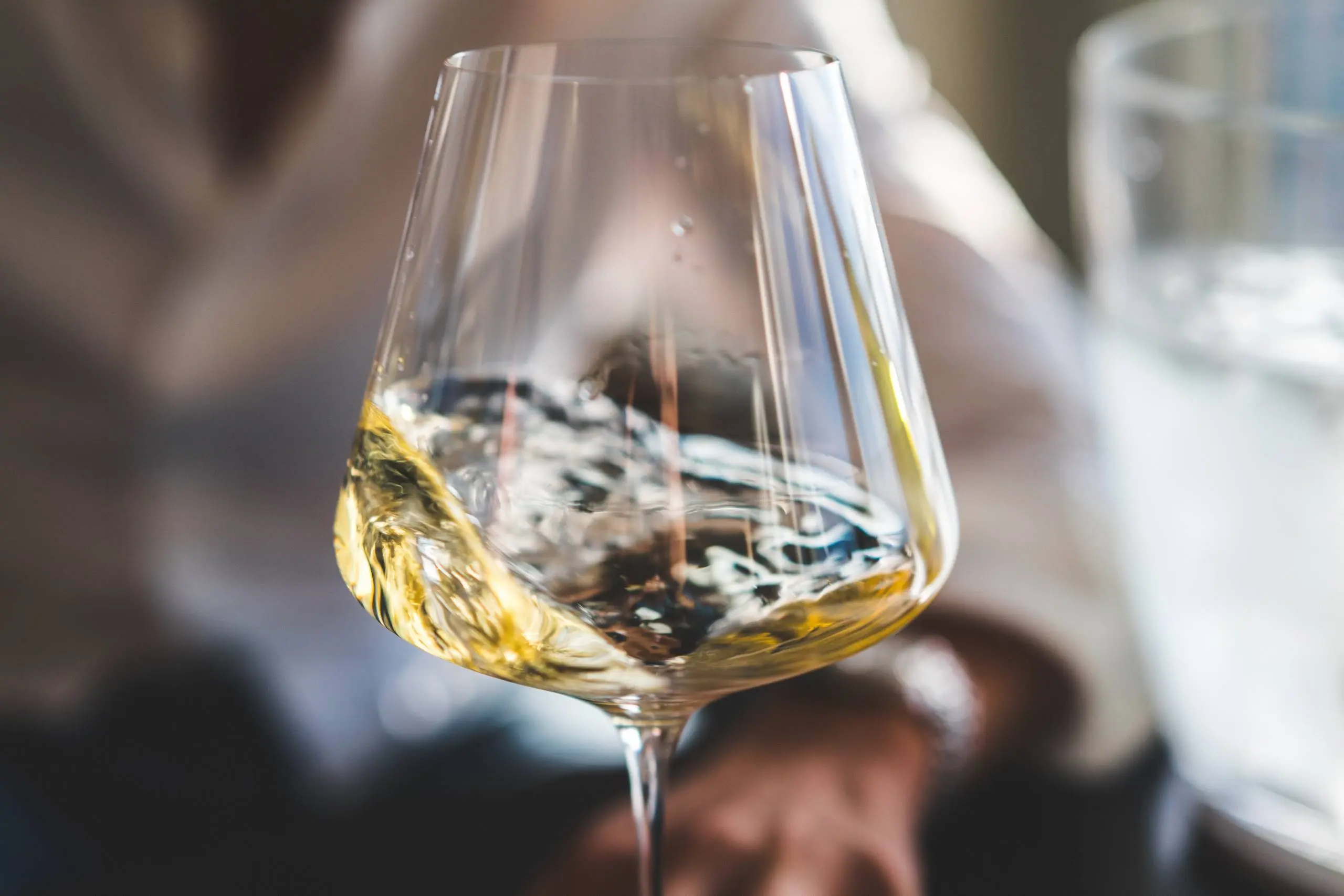 Glass of white wine being held outdoors with a yacht visible in the background.