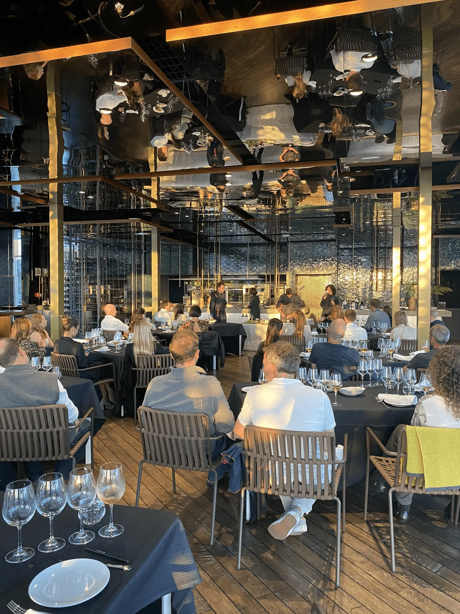 Formal dining event in a modern restaurant with guests seated at tables overlooking a marina at night.