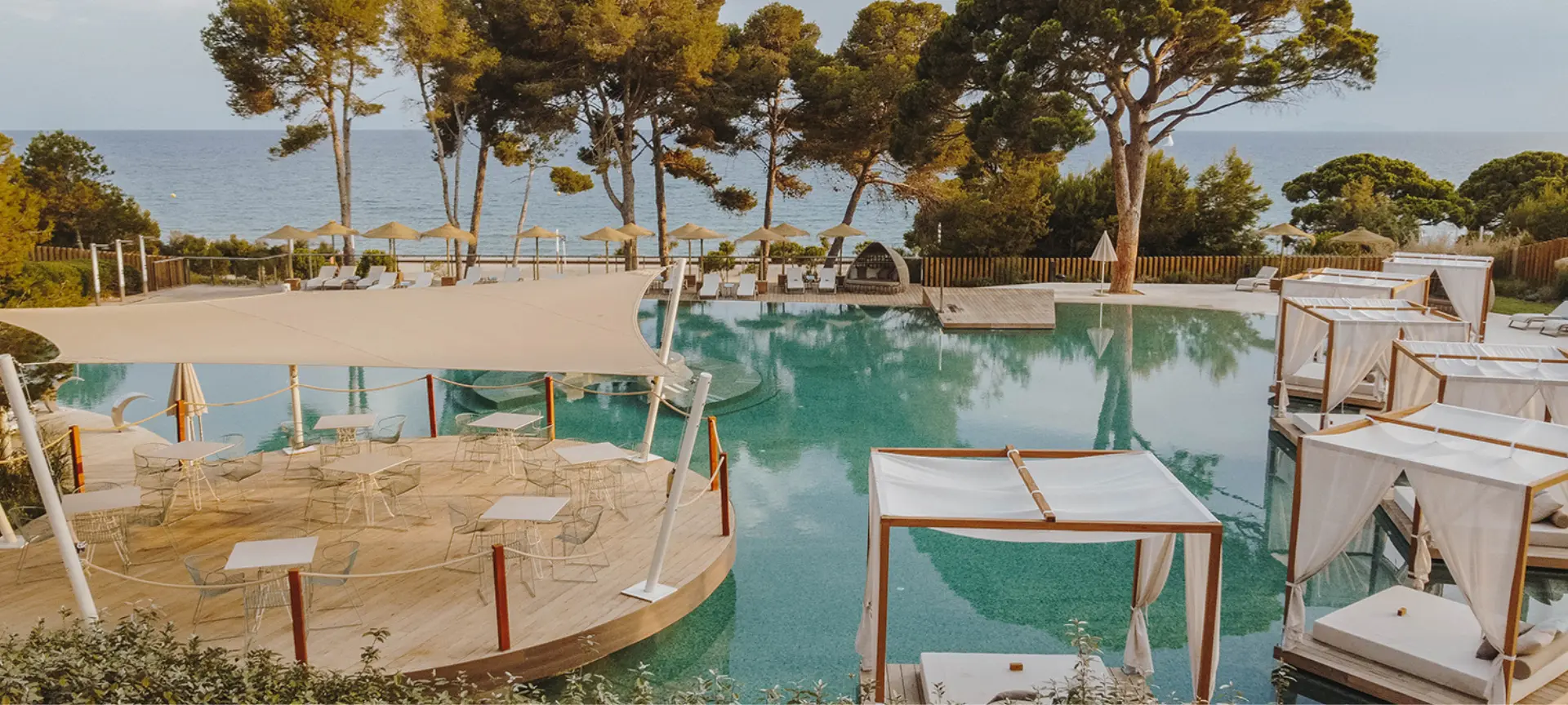 Beach club with a poolside relaxation area, outdoor tables and daybeds overlooking the sea, surrounded by nature on the Costa Dorada near Barcelona.